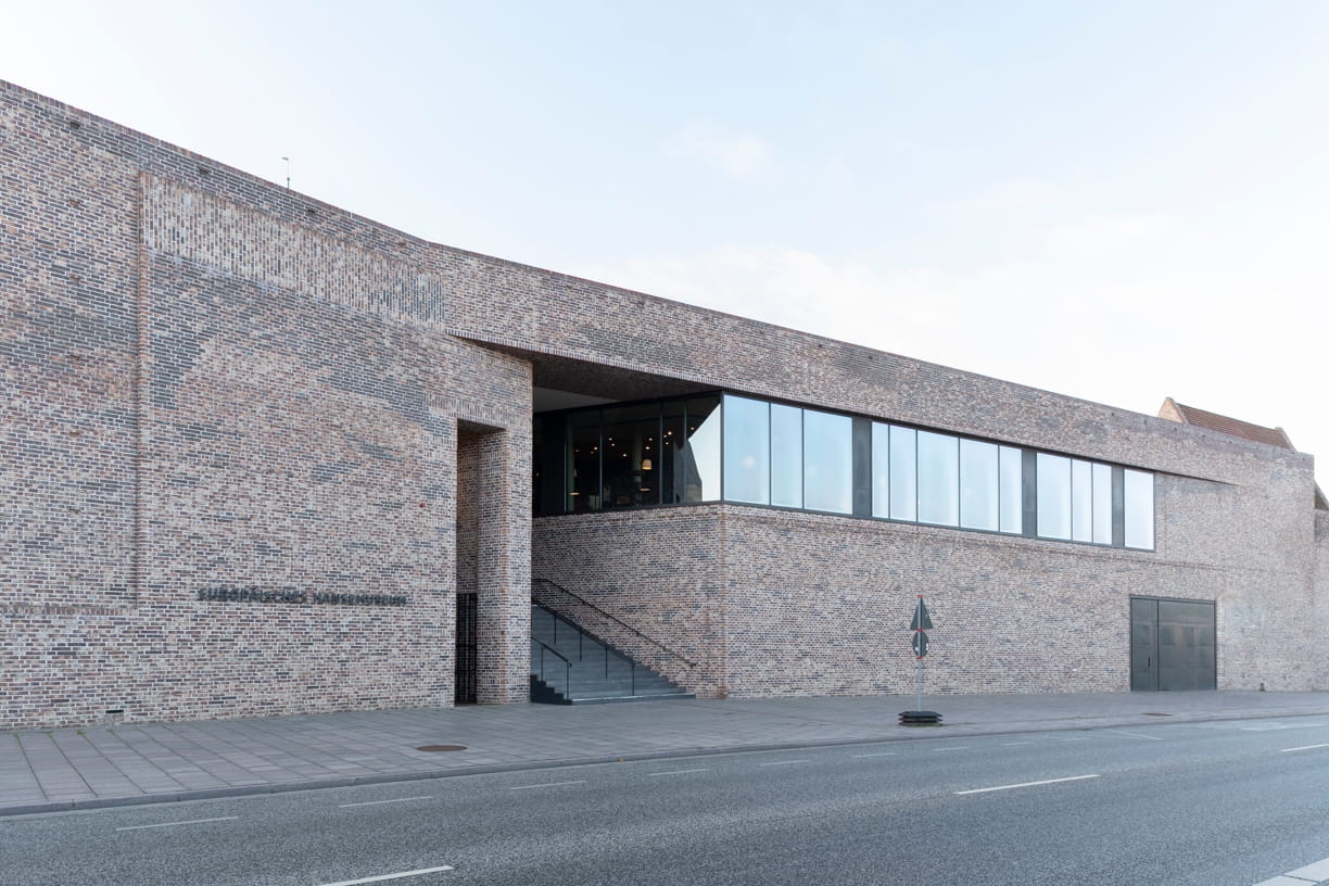 Blick von der Straße auf die rote Backsteinfassade und die Treppe des Europäischen Hansemuseums von Andreas Heller Architects in Lübeck