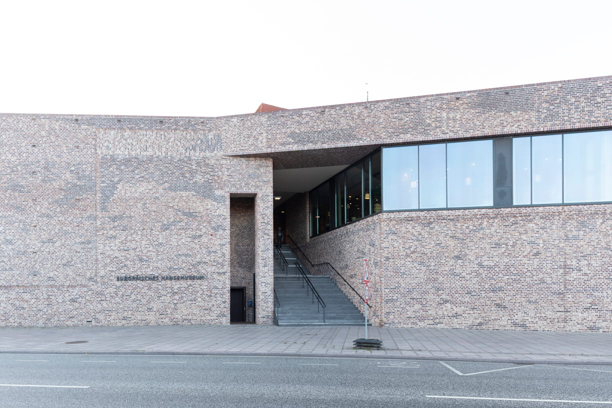 Blick von der Straße auf die rote Backsteinfassade und die Treppe des Europäischen Hansemuseums von Andreas Heller Architects in Lübeck.